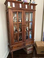 Front view of wood cabinet with glass paneled doors, two drawers at bottom, standing on legs, includes key on door lock.