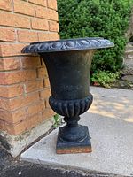 Front angle of cast iron urn planter showing decorative scalloped design and square base