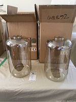 Two glass shades for ceiling lamps with brown tint, placed in front of original boxes.