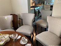 Four fabric upholstered dining chairs around a wooden table in a dining area, showing upholstery pattern and dark wooden legs.