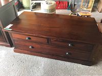Front view of wood veneer coffee table showing four drawers with black metal cup pulls and medium brown finish
