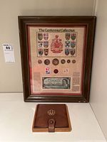 Framed Centennial Collection with coins, Canadian dollar bill and stamps alongside leather coin pouch on table
