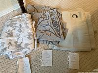 Three sets of curtain panels on carpet: beige floral, gray botanical, and light beige with grommets; handwritten notes in front