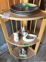 Three shelves showing plates on top, ceramic swan and cat figurines in middle shelf, small figurines on bottom shelf.