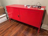 Front view of red metal file cabinet showing two doors with vents and lock with key.