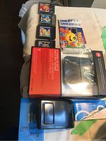 Top view of four Game Boy Color cartridges, with two boxed Bluetooth speakerphones and instruction manuals on a bed