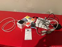 Apple iPod Nano and Samsung YP-T7 MP3 player with various cords, manuals, and accessories on a red surface.