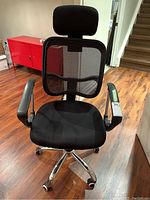 Front view of black office chair showing padded headrest, mesh backrest, armrests, and caster wheels on chrome base.
