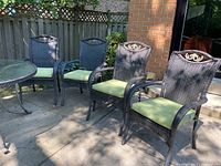 Set of four patio chairs positioned together outdoors on a patio with a round glass table partially visible.