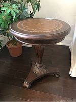 Full view of the round wooden pedestal side table showing the inlay design on the top surface and overall shape.