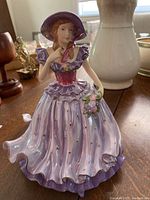 Front view of Royal Doulton Julia figurine in purple dress and hat, showing ruffled layers and floral bouquet.