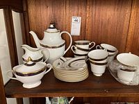 Full set displayed on wooden shelf showing teapot, creamer, sugar bowl, teacups, and saucers with one saucer visibly broken.