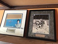 Two framed sports memorabilia items on a shelf, one with hockey signatures and the other with racing theme.
