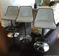 Front view of three white faux leather swivel bar stools with chrome bases and footrests.
