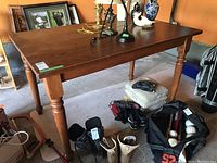 Photo of rectangular wood veneer counter-height table with carved legs showing some marks, with various items and shoes underneath and on top.