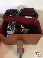 Camera and lens inside an open brown leather hard case with dark red fabric interior lining. Damage visible to case.