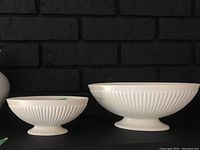 Front view of two white ridged Wedgwood jasperware oval footed bowls, one smaller and one larger.
