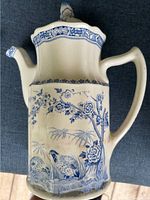 Front view of antique coffee/chocolate pot showing blue floral and quail pattern on cream ceramic. Scalloped edge lid and curved handle visible.