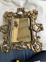 Full front view of antique metal framed mirror showing ornate design, glass, and frame condition.