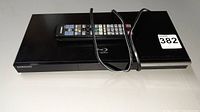 Top angled view of Samsung BD-C5500T Blu-ray player with remote and power cord laying on top