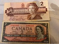 Both Canadian two dollar notes, 1986 on top and 1954 below, showing front sides with Queen Elizabeth II portraits and denomination markings.