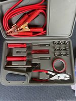 Complete car tool set in case showing jumper cables, screwdrivers, pliers, wrench sockets, electrical tape, and tire pressure gauge.