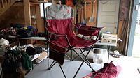 Full view of oversized red and grey foldable camping chair with metal frame set up indoors on a table.