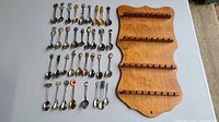 Full spread of all 33 collector spoons laid out on a flat surface next to the wooden rack, showing arrangement and quantity.