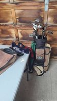 Photo of full golf bag standing on floor beside a table, showing clubs and bag overall.