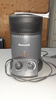 Front view of Honeywell Surround Heater showing mesh grille top, control panel with rotary knobs and power light, power cord coiled in front.