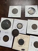 Overview of the 8 old coins housed in white cardboard holders with country and date handwritten on each.