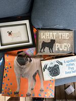 Overview photo of lot showing all four items: two wooden signs, framed pug picture, and large pug paper gift bag