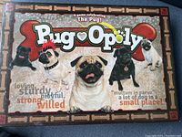 Photo of Pugopoly board game box showing front cover with pug images and bone decorative border.