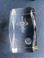 Clear glass rectangular paperweight with beveled edges showing laser-etched 3D satellite, Earth, and stars images inside