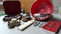 Overview of lot showing antique serving utensils, silver plate cutlery in red case, spoon holders, silver bowls, and glass drip protectors.