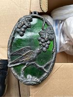 Full view of dark green stained glass sun catcher with metal bird and grape decoration