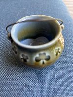 Close-up of the miniature ceramic cauldron showing clover stamped details, wire handle, and leg support.