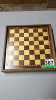 Top view showing pressed wood chessboard with alternating light and dark squares and decorative inlaid border.