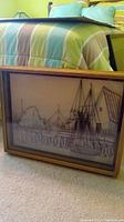 Photo showing framed 3-D harbor scene artwork with string art sailboat resting against a bed with a striped bedspread.
