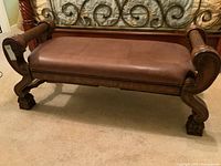 Side angled view showing leather cushion seat and carved wood armrest and legs.