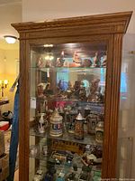 Front view of the filled cabinet showing wood grain frame, glass shelves, illuminated interior, and glass side doors