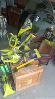 Multiple Ryobi cordless yard tools (chainsaw, blower, trimmer/edger) arranged on wooden crate