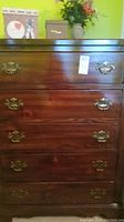 Full front view of the wooden chest of drawers with five drawers and brass handles.