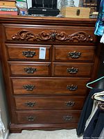 Front view of wooden 6 drawer chest with metal handles and detailed carved top drawer.