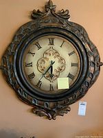 Full view of the decorative quartz wall clock with bronze ornate frame showing Roman numerals and central vine design.