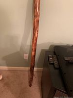 Full length of wooden didgeridoo leaning against a wall near a TV stand showing natural wood grain and polished surface.