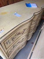 Top angled view showing curved top surface, scratches, and gold floral details on drawer fronts.