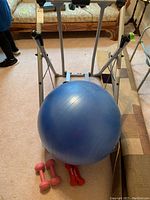 Tony Little Gazelle Edge exercise machine with a large blue balance ball and pairs of small hand weights underneath.