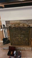 Full view showing cast iron fireplace toolset on left side and decorative brass fireplace screen on fireplace opening.