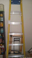 Full view of yellow fiberglass ladder showing aluminum steps, approximately seven feet tall.